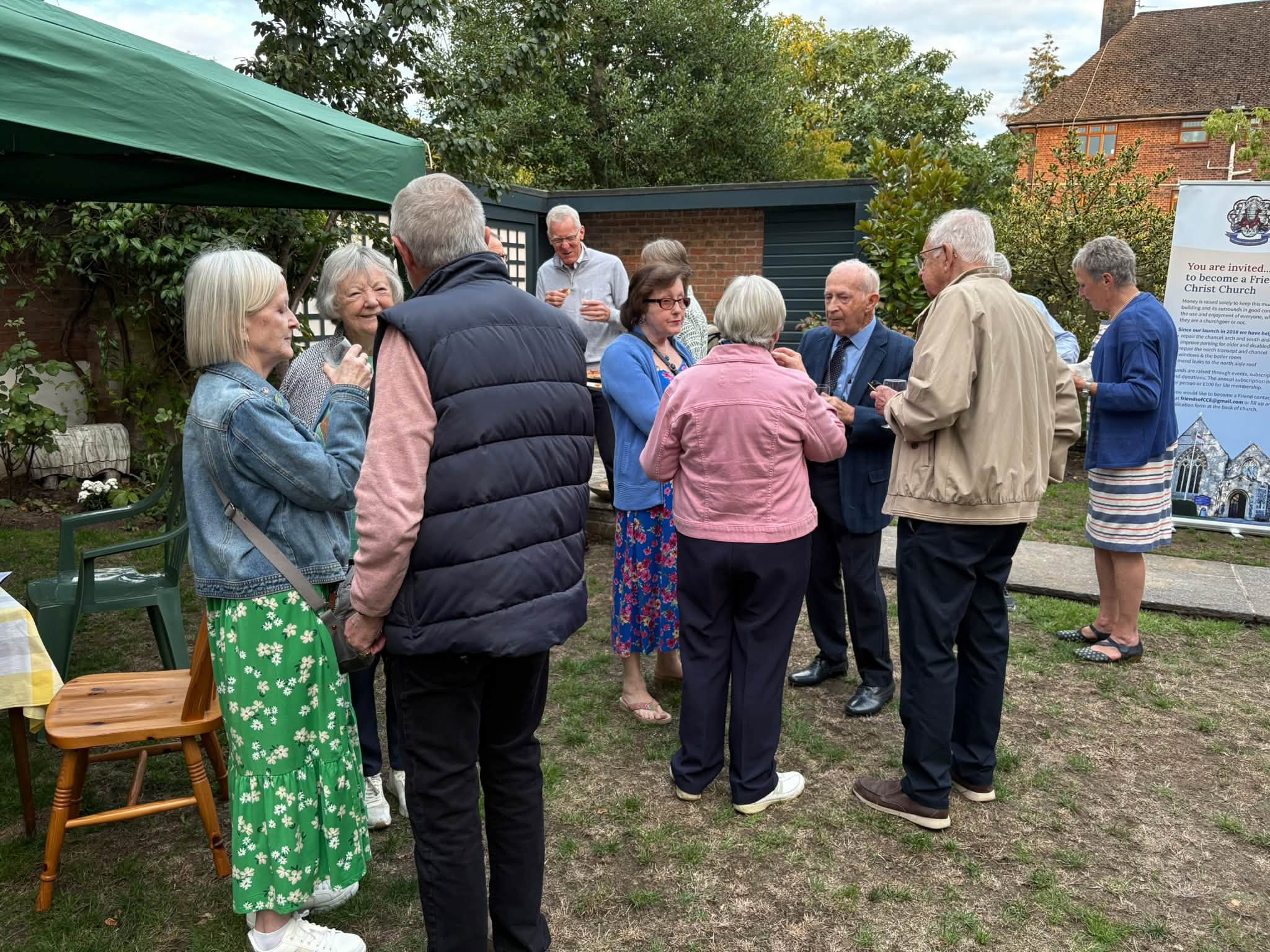 Group of people standing around in a garden chatting, holding glasses of drink