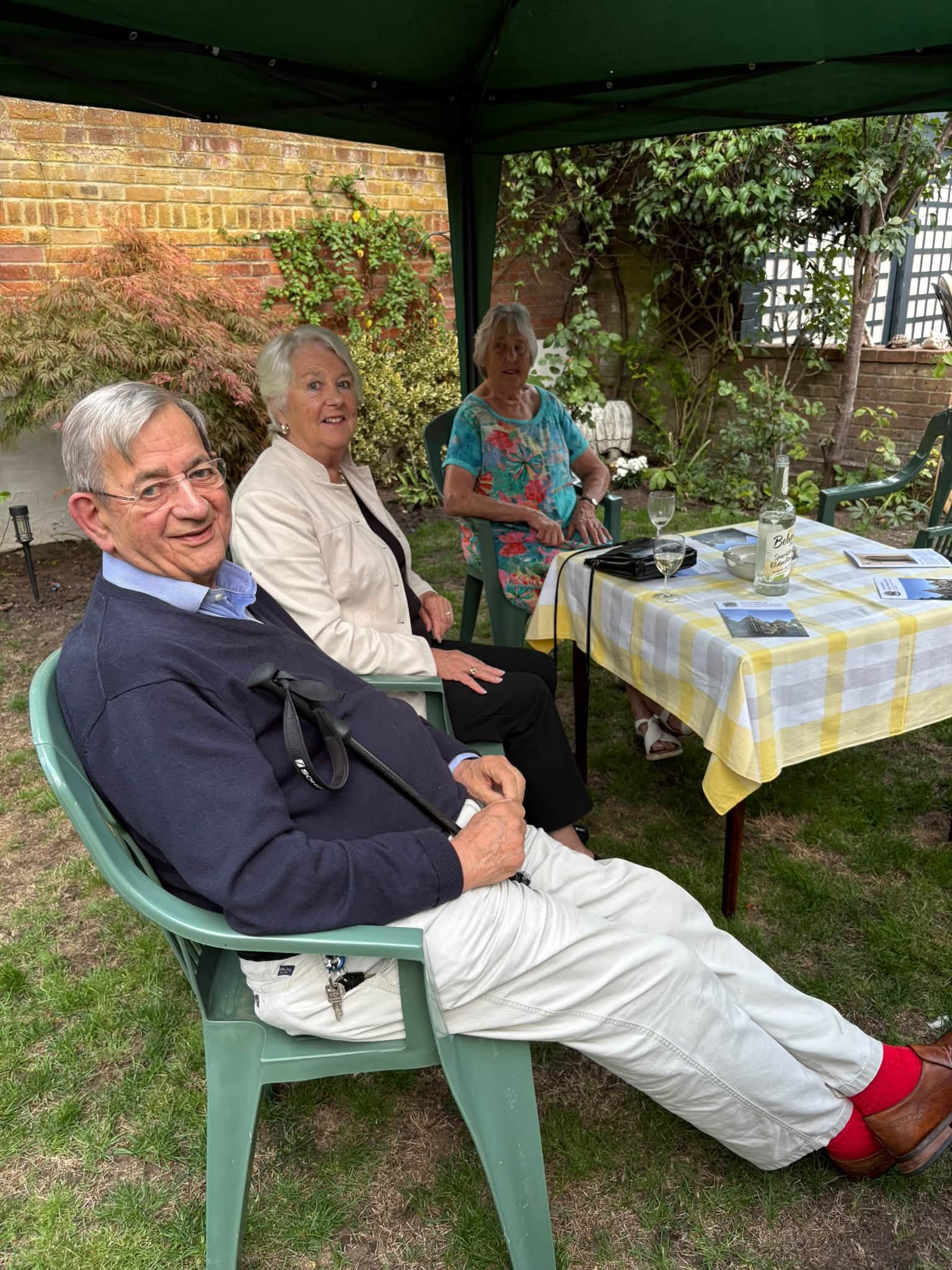 3 people sitting round a small table under a gazebo. There are drinks of wine and juice on the table