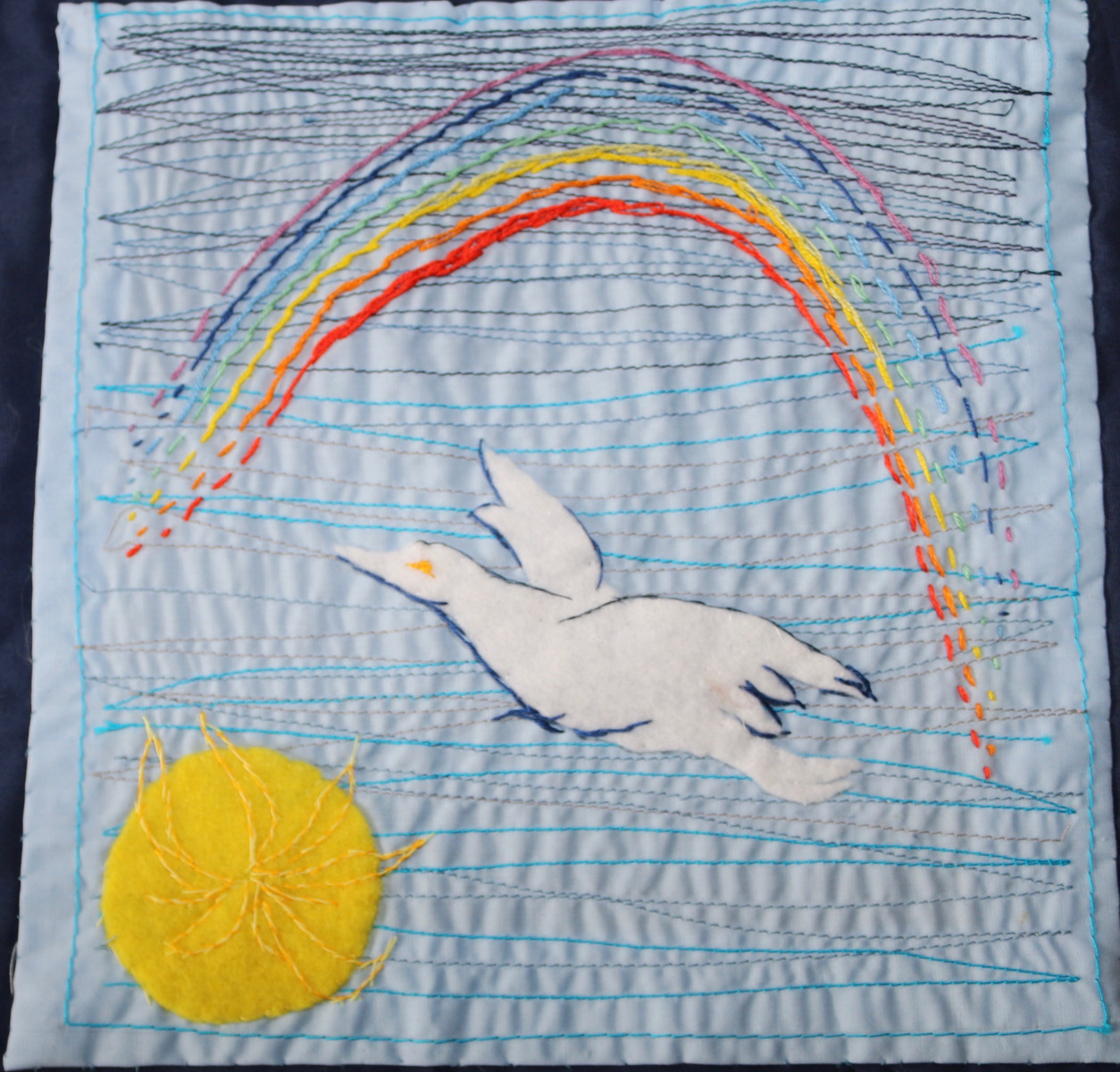 Image, created in embroidery, of a sun, dove and a rainbow