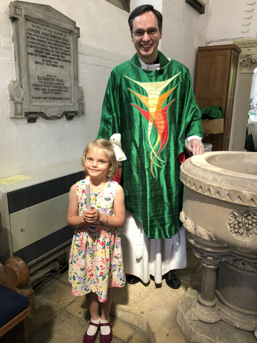Young girl stands next to a vicar and the font. She is holding a lit candle.